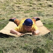 Child sliding down grassy hill on piece of cardboard
